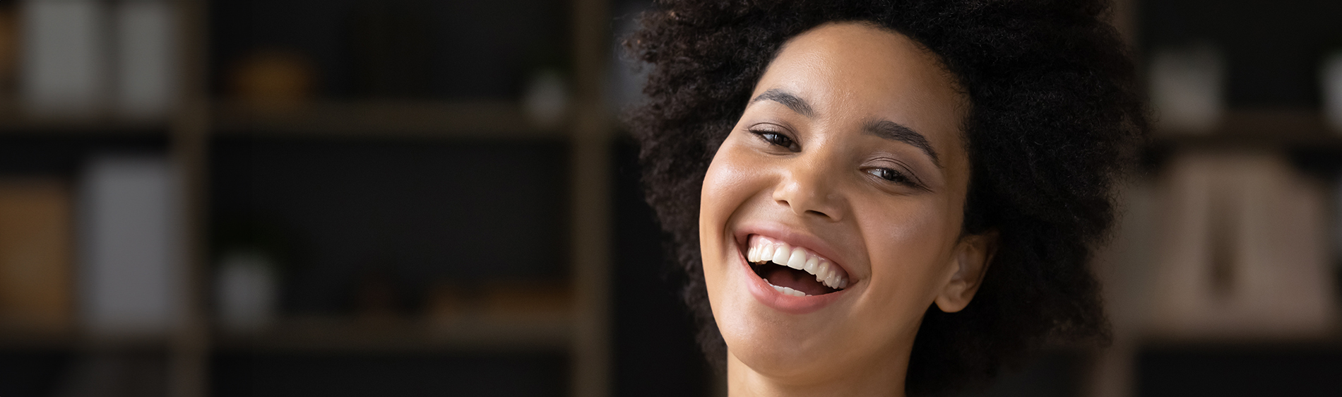 The image is a photograph of a woman with light skin, smiling at the camera. She appears to be in her late twenties or early thirties and has long hair. Her eyes are looking directly at the camera, and she is holding up her index finger near her mouth as if she s making a point or emphasizing something. The background is plain and light-colored, which suggests that this could be a stock photo used for various purposes such as advertising, personal branding, or lifestyle content.